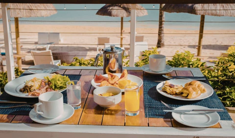 coconut-club-on-stocking-Island | Hideaways Beach Resort Exuma, GeorgeTown Vacation Rentals Beachside breakfast table set for two on a balcony with plates, fruit, bread, and beverages against the ocean view.