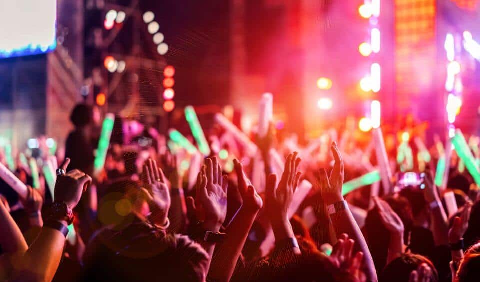 night-life-and-events | Hideaways Beach Resort Exuma, GeorgeTown Vacation Rentals Crowd of concertgoers raising hands in a neon-lit stage scene with colorful lights at a live show.